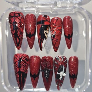 May include: A set of ten red glitter press-on nails with various black and white designs. The designs include a spiderweb, a bat, a character illustration, and a rose. The nails are almond-shaped and displayed in a clear plastic case.