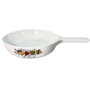 May include: White ceramic skillet with a long handle. The skillet features a colorful fruit and vegetable design along the rim, with the text "Le Persil" below the design. The skillet is designed for cooking.