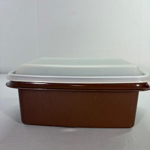 May include: A rectangular brown food storage container with a clear, slightly frosted lid. The lid has a white rim that fits snugly around the container's edge. The container is made of a durable plastic material.