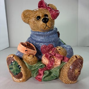 May include: A ceramic teddy bear figurine with a blue sweater, a pink bow, and a heart-shaped gift. The bear is holding a small bowl and has green and brown accents. The figurine is approximately 8 inches tall.