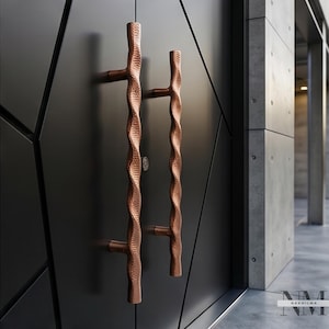 May include: Two vertical door handles with a textured, hammered copper finish and a wavy, organic shape. These handles are mounted on a matte black door featuring a geometric panel design with sharp, angular lines and a small circular lock.