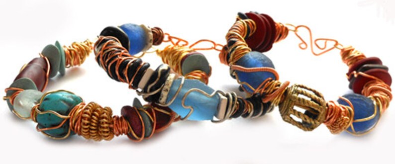 Pode incluir: Tr&ecirc;s pulseiras artesanais com um estilo bo&ecirc;mio. Cada pulseira apresenta uma combina&ccedil;&atilde;o &uacute;nica de contas em v&aacute;rias cores, incluindo turquesa, azul, vermelho e preto, enroladas com fio de cobre. As pulseiras s&atilde;o exibidas em um fundo branco.