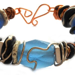 Pode incluir: Pulseira artesanal com contas azuis, pretas e brancas, com detalhes em fio de cobre e prata. A pulseira inclui uma grande conta facetada azul clara no centro. Fecho de gancho e argola em cobre.