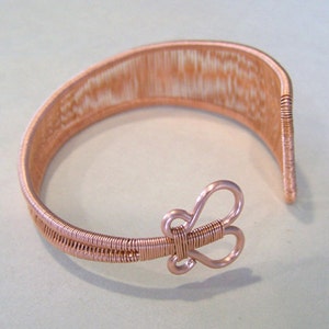 Op de afbeelding: Een koperkleurige draadmanchetarmband. De armband heeft een geweven ontwerp en een vlindervormige sluiting. Het open manchetontwerp maakt het gemakkelijk te dragen. De armband is gemaakt van kopersnoer.