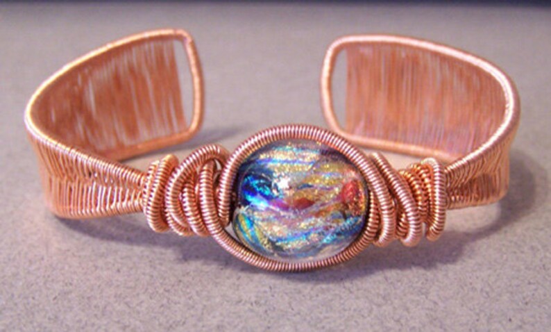 Puede incluir: Pulsera de pu&ntilde;o de alambre de cobre con una cuenta de vidrio dicroico. La pulsera presenta un dise&ntilde;o de alambre tejido con una cuenta de vidrio colorida en el centro. El dise&ntilde;o de pu&ntilde;o abierto permite un f&aacute;cil uso.