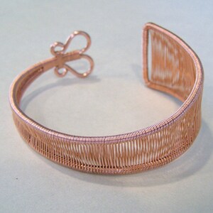 Op de afbeelding: Koperkleurige draadmanchetarmband. De armband heeft een geweven ontwerp met een vlindervormige sluiting. Het open manchetontwerp maakt het gemakkelijk te dragen. Een uniek sieraad.