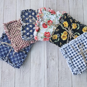 May include: A set of eight fabric squares with frayed edges. The squares are in various patterns, including gingham, floral, and stars. The squares are tied together with twine.
