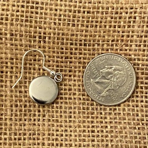 Puede incluir: Un pendiente de plata con un colgante redondo. El pendiente se muestra junto a una moneda de 25 centavos de d&oacute;lar estadounidense para comparar el tama&ntilde;o.