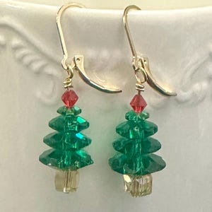 May include: A pair of gold dangle earrings featuring green crystal Christmas tree charms with red crystal accents.