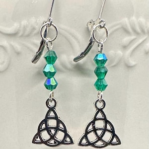 May include: A pair of silver-toned dangle earrings. Each earring features a Celtic knot charm, three faceted green beads, and a decorative hook. The earrings are designed for pierced ears and are displayed against a white background.