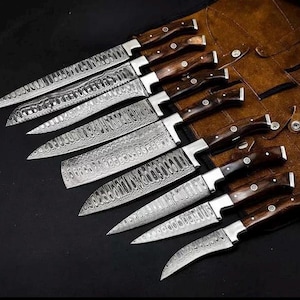 Peut inclure: Un ensemble de huit couteaux de cuisine avec des lames en acier damass&eacute; au motif ondul&eacute; et des manches en bois brun fonc&eacute; avec des rivets argent&eacute;s, dispos&eacute;s en diagonale sur un &eacute;tui en cuir brun avec des fermetures &agrave; pression et des coutures.