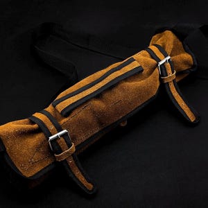 Peut inclure: Un &eacute;tui &agrave; outils en cuir su&eacute;d&eacute; beige dot&eacute; de sangles en nylon noir, de bordures en cuir noir et de deux boucles m&eacute;talliques argent&eacute;es. Cet &eacute;tui de rangement cylindrique comprend une longue sangle noire r&eacute;glable et deux fermetures &agrave; boucle.