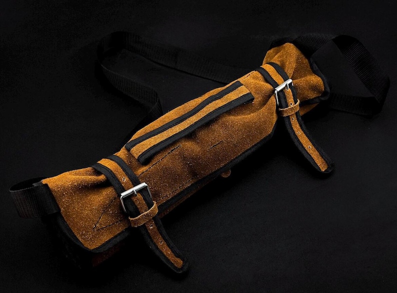 Peut inclure: Un &eacute;tui &agrave; outils en cuir su&eacute;d&eacute; beige dot&eacute; de sangles en nylon noir, de bordures en cuir noir et de deux boucles m&eacute;talliques argent&eacute;es. Cet &eacute;tui de rangement cylindrique comprend une longue sangle noire r&eacute;glable et deux fermetures &agrave; boucle.