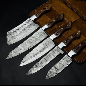 Peut inclure: Un ensemble de cinq couteaux de cuisine avec des lames en acier Damas pr&eacute;sentant un motif ondul&eacute; en couches. Chaque couteau poss&egrave;de un manche en bois brun fonc&eacute; avec des incrustations m&eacute;talliques florales et des rivets en laiton.