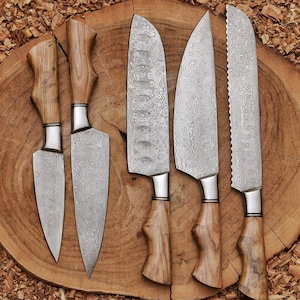 Peut inclure: Un ensemble de cinq couteaux de cuisine dot&eacute;s de lames en acier damas &agrave; motifs et de manches en bois brun clair. Les couteaux pr&eacute;sentent des formes de lame vari&eacute;es, incluant des bords pointus, incurv&eacute;s et dentel&eacute;s, avec une texture m&eacute;tallique ondul&eacute;e.