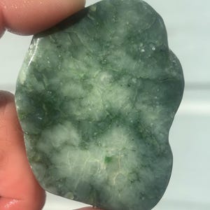 May include: A polished, irregular, flat stone featuring a mottled surface with varying shades of forest green, sage, and translucent white. The mineral specimen displays a crystalline, marbled texture with visible internal fractures and inclusions.