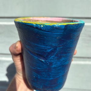 May include: Hand-painted blue ceramic planter with a textured surface. The rim features a colorful design with pink, yellow, and turquoise accents. This decorative pot is ideal for small plants and adds a pop of color to any space.