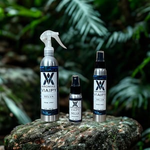 May include: Three silver spray bottles of varying sizes, labeled "Aromas Viaipy Selva Room Spray," are displayed on a mossy rock against a backdrop of green foliage. The bottles have a blue and white label with a distinctive logo.