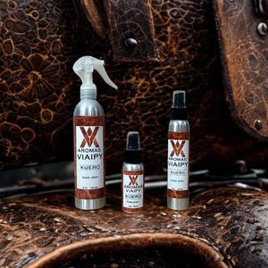 May include: Three silver spray bottles of varying sizes are displayed. Each bottle has a white label with the text "Aromas Viaipy Kuero" and a brown and white logo. The bottles are set against a textured brown leather background.