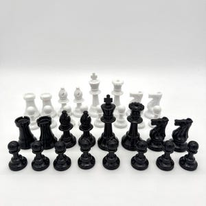 May include: A complete chess set with black and white pieces. The set includes pawns, rooks, knights, bishops, a king, and a queen. The pieces are arranged on a white surface, ready for a game of chess.