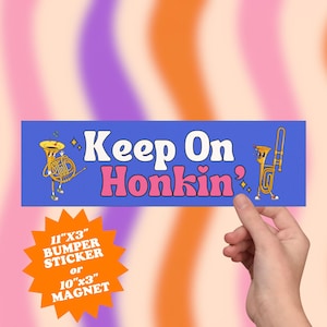 May include: A blue bumper sticker or magnet with the text "Keep On Honkin'" in white and pink. The sticker features cartoon illustrations of musical instruments and is 11"x3" or 10"x3".