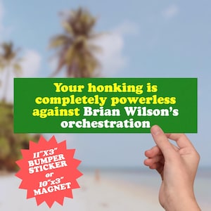 Könnte beinhalten: Ein grüner Aufkleber mit gelbem Text: „Ihr Hupen ist völlig machtlos gegen Brian Wilsons Orchestrierung.“ Ein roter Stern weist darauf hin, dass der Aufkleber 28 cm x 8 cm oder ein Magnet von 25 cm x 8 cm groß ist.