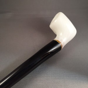 May include: A white ceramic pipe with a black stem. The pipe has a gold trim around the bowl.