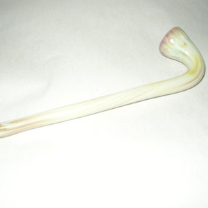 Puede incluir: Una pipa de vidrio blanco con un tallo curvo y una boquilla bulbosa. El vidrio tiene un patrón de remolino en tonos amarillos y rosados.