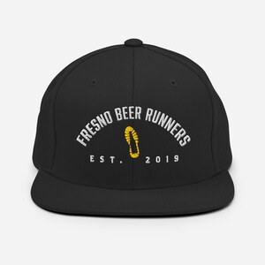 Könnte beinhalten: Schwarze Baseballkappe mit flachem Schirm. Der weiße Text "FRESNO BEER RUNNERS" ist in einem Bogen angeordnet, darunter eine gelbe Fußabdruckgrafik. Darunter steht der Text "EST. 2019".
