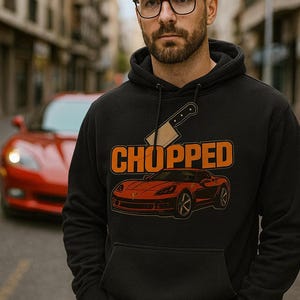 May include: Black hoodie featuring the word "CHOPPED" in orange, a red sports car graphic, and a cleaver design. The hoodie is worn by a person wearing glasses, with a red sports car visible in the background.