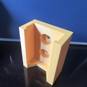May include: A light orange, 3D-printed, L-shaped object with two circular holes. The object is made of a solid material and has a smooth surface. The background is a textured blue.