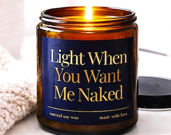 May include: A lit soy wax candle in a brown glass jar with a navy blue label. The label reads "Light When You Want Me Naked" in gold lettering. The candle is made with natural soy wax and made with love.