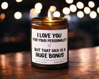 Puede incluir: Una vela encendida en un frasco de vidrio marrón con una etiqueta blanca. La etiqueta dice "I LOVE YOU FOR YOUR PERSONALITY BUT THAT DICK IS A HUGE BONUS." La vela está hecha con cera de soja natural.