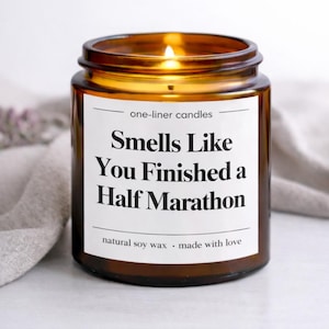 May include: A burning amber glass candle with a white label. The label says "Smells Like You Finished a Half Marathon." The candle is labelled "one-liner candles" and "natural soy wax - made with love."