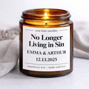 Könnte beinhalten: Ein brennendes bernsteinfarbenes Glas-Kerzenglas mit einem weißen Etikett. Auf dem Etikett steht "No Longer Living in Sin" mit den Namen "EMMA & ARTHUR" und dem Datum "12.13.2025". Der Text "natural soy wax • made with love" steht ebenfalls auf dem Etikett.