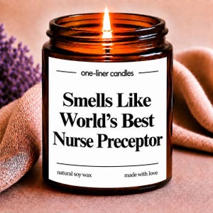 May include: A lit candle in a brown glass jar with a white label that reads one-liner candles, Smells Like World's Best Nurse Preceptor, natural soy wax, and made with love. The candle features a visible flame and is filled with natural soy wax.