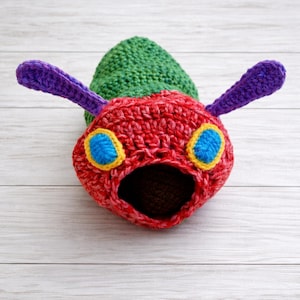 May include: A handmade crochet caterpillar hat in vibrant colors. The hat features a red head with blue and yellow eyes, purple antennae, and a green body. The open mouth design adds a playful touch to this whimsical accessory.