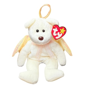 May include: A white plush dog toy with iridescent wings and a pink ribbon. The dog has black eyes and a brown nose. A red heart-shaped tag is attached to the dog's ear.