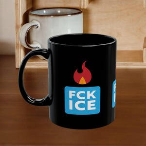 May include: Black ceramic mug featuring the text "FCK ICE" in white and blue, with a flame icon. A second white mug is visible in the background, along with a wooden shelf.