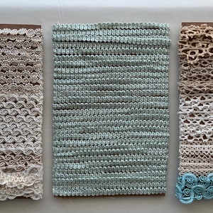 May include: Three pieces of trim, each on a brown card. The trim on the left is white and has a scalloped edge. The trim in the middle is light blue and has a woven texture. The trim on the right is beige and has a variety of lace patterns.