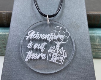 May include: Clear acrylic pendant necklace with the phrase "Adventure is out there" and a house with balloons design. The pendant hangs from a black cord.