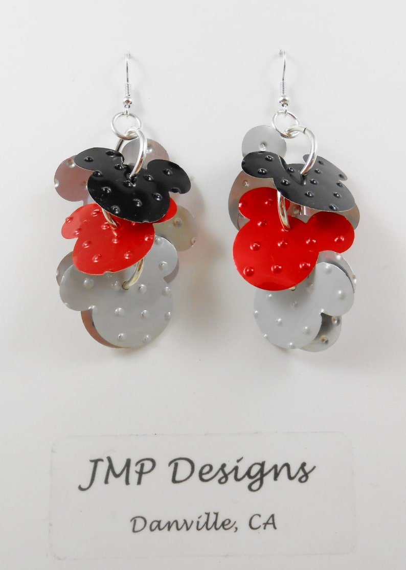 Puede incluir: Pendientes colgantes con dise&ntilde;o de cabeza de Mickey Mouse en metal rojo, negro y plateado. Los pendientes tienen cierre de poste. El texto "JMP Designs Danville, CA" es visible. Un accesorio divertido.