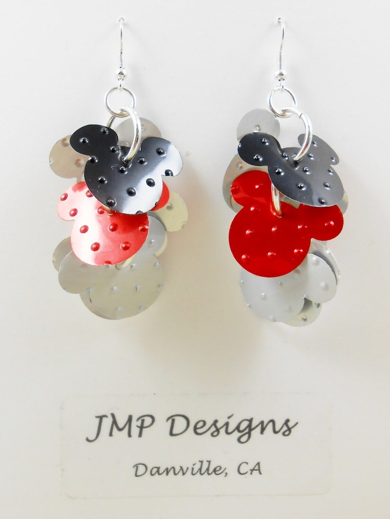 Puede incluir: Pendientes hechos a mano con un dise&ntilde;o de Mickey Mouse. Los pendientes son de metal plateado con detalles en rojo y negro. Cuelgan de ganchos plateados. El texto "JMP Designs Danville, CA" es visible.