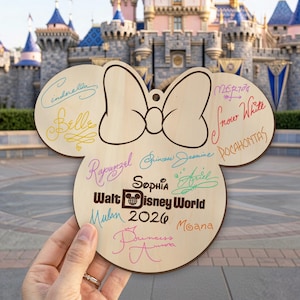 May include: A light-colored wooden cutout shaped like a mouse head with a bow, featuring colorful printed signatures of Disney princesses including Cinderella, Belle, Rapunzel, and Ariel, plus the text "Sophia", "Walt Disney World", and "2026".