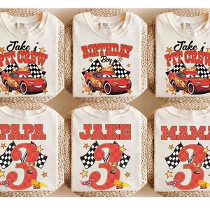 Puede incluir: Seis camisetas de color blanco roto con gr&aacute;ficos de coches de carreras rojos con el n&uacute;mero 95, banderas a cuadros y estrellas. Tres camisetas muestran 'Jake's Pit Crew' o 'Birthday Boy', y tres muestran 'PAPA', 'JAKE' o 'MAMA' con un n&uacute;mero 3 grande.