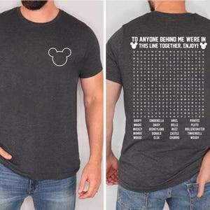 May include: Dark gray t-shirt with a white Mickey Mouse outline on the front. The back of the shirt features a word search with Disney-themed words and the text "TO ANYONE BEHIND ME WERE IN THIS LINE TOGETHER. ENJOY!"