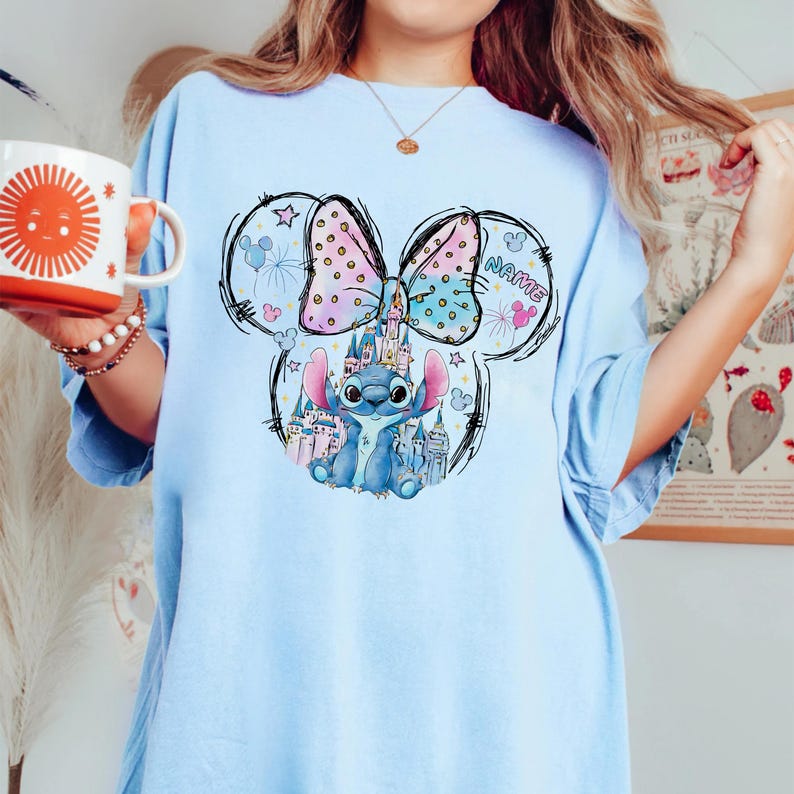 Pu&ograve; includere: T-shirt azzurra con una grafica a cartoni animati di Stitch, un castello e un fiocco. Il fiocco ha pois rosa e blu e la parola "NAME" &egrave; stampata sull'orecchio destro. La maglietta &egrave; uno stile casual e confortevole.