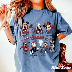 May include: A blue jean coloured t-shirt with a graphic of Disney characters as Avengers. The design includes Mickey Mouse, Minnie Mouse, Goofy, Pluto, Daisy Duck, Donald Duck, and Chip and Dale. The word "AVENGERS" is also displayed.