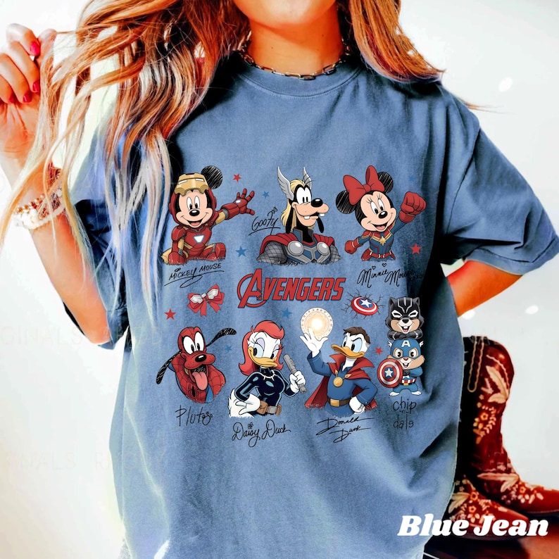 May include: A blue jean coloured t-shirt with a graphic of Disney characters as Avengers. The design includes Mickey Mouse, Minnie Mouse, Goofy, Pluto, Daisy Duck, Donald Duck, and Chip and Dale. The word "AVENGERS" is also displayed.