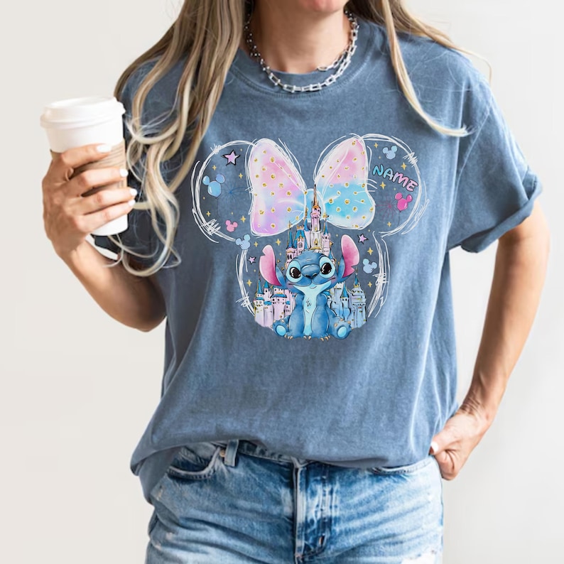 Pu&ograve; includere: T-shirt blu con grafica di Stitch di Lilo & Stitch, un castello e un fiocco dai colori pastello. Il design include la parola "NAME" e le orecchie di Topolino.